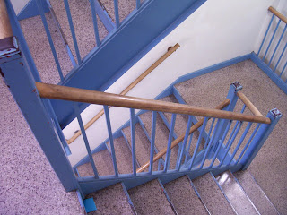Looking down a grey staircase with distressed blue metal balusters and wooden handrail