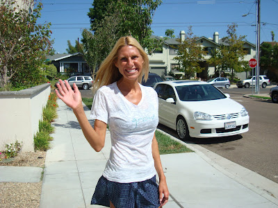 Woman in white shirt and skirt waving on sidewalk