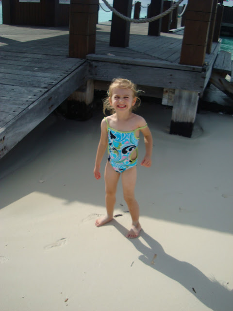 Young girl standing in sand smiling in swimsuit next to pier
