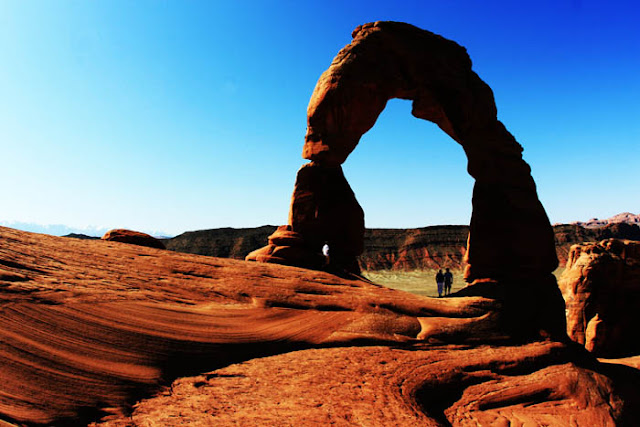 Two people standing underneath Delicate Arch at Arches National Park in southwest Utah.