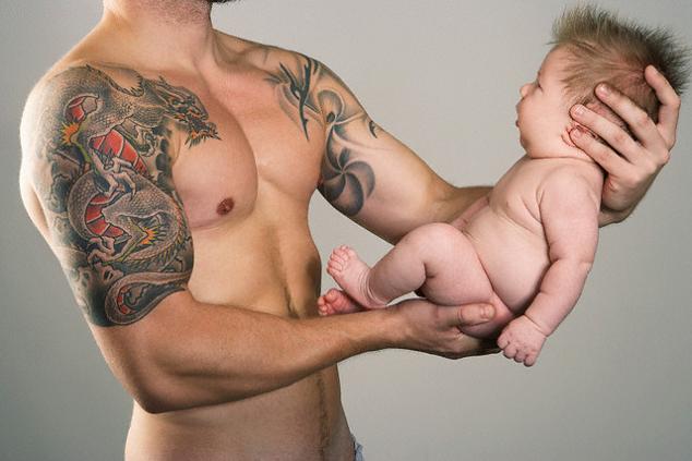 New father with arm dragon tattoo holding his newborn baby.