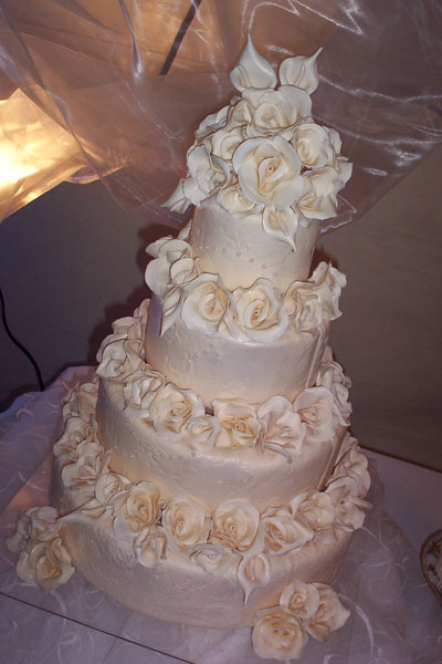 Four tier white wedding cake with sugar roses separating each tier