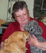 photo of Carol holding Puddle, her gray poodle, as Sophie looks on