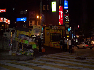 A cart vendor sells fruit and other items at night in Gangnam