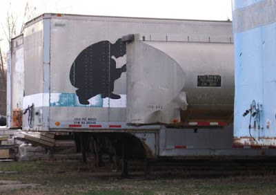 Crouching silhouette on the side of a semi trailer, shot so it looks like he's doing something to the adjacent trailer