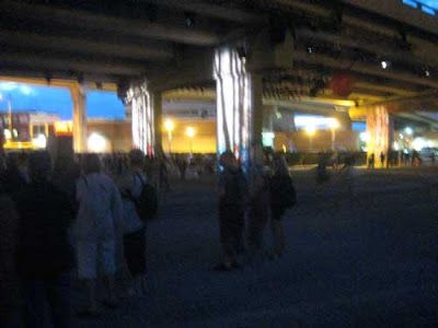 5 story-tall highway overpass at night, shot from below, with crowds of people under it