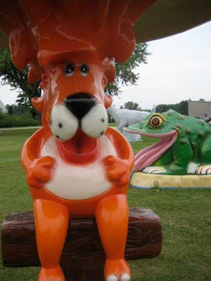 Orange cartoonish lion. Green frog in the background appears to be licking the lion's elbow.