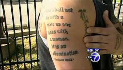 Man showing his right arm, tattoed in blackletter Thou shalt not lie with a male as one does with a woman. It is an abomination. Leviticus 18.22