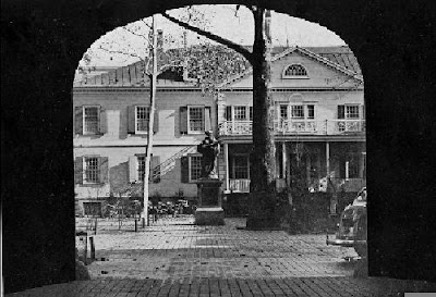 Black and white photo through a darkened archway, courtyard with statue and colonial-style building in background