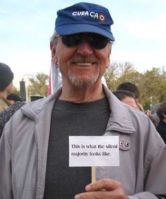 60ish white man holding a tiny sign that says This is what the silent majority looks like