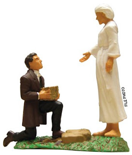 A toy of Joseph smith sitting on his knees and Moroni with white dress while he giving Golden plates to Joseph Smith photo