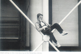 Seorang badut sedang duduk pada “cross bracing” pada bangunan Pompidou Centre