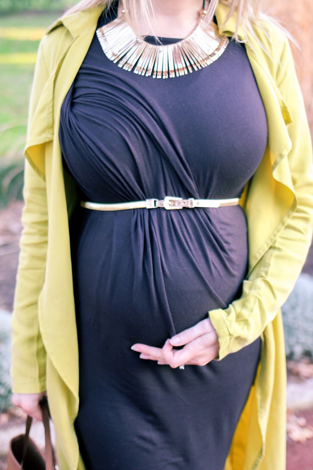 The Goldfields Girl styling maternity fashion. She wears black maternity dress, green jacket, statement gold necklace, brown boots and Michael Kors bag.