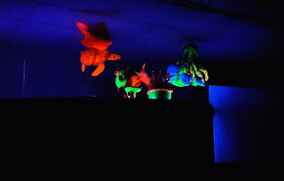 Teatro de luz negra com figuras de peixes feitas em tecido de espuma e pintadas com tinta fluorescente.