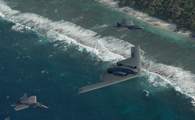 Two F-22 Raptors and a B-2 Spirit bomber deployed to Andersen Air Force Base, Guam, fly in formation over the Pacific Ocean