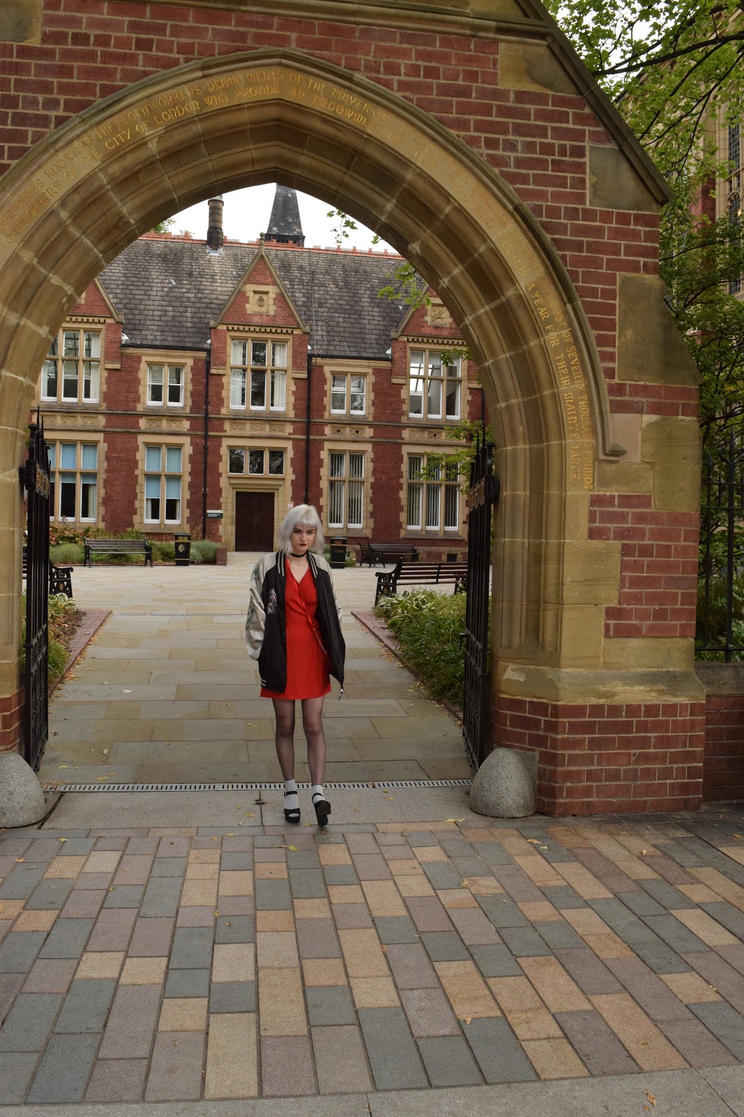 silver haired girl in red dress, heels and sukajan standing in an archway at the University of Leeds