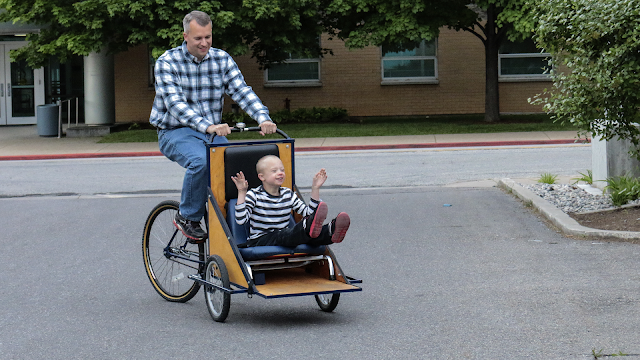 Photo of Parker, smiling, as he rides with his dad in the new bike.