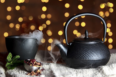 black teacup and teapot, backlit by strings of lights