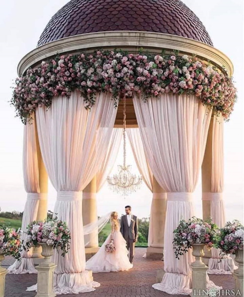Se você conhece o autor desta imagem, por favor nos informe para que possamos atribuir-lhe os devidos créditos. Obrigado. Casal de noivos num cenário decorado com flores e véus.
