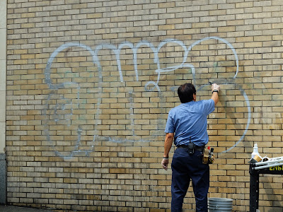 a member of building maintenance removing graffiti on the side of Hotel Max in downtown