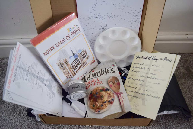 A packing box open showing the contents including a 3d model of Notre Dame De Paris and a paint by numbers set