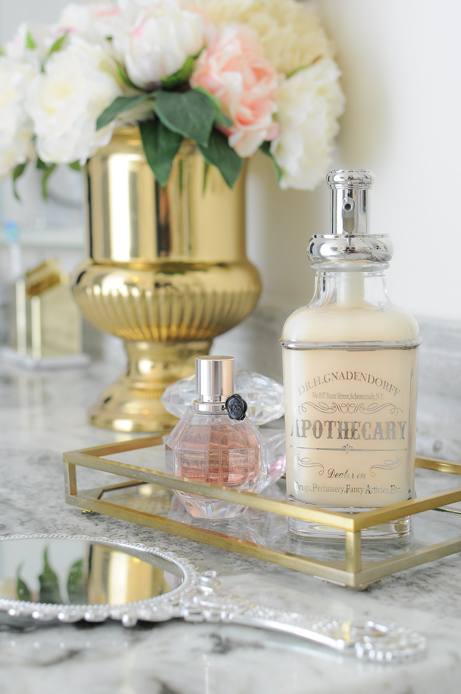 Feminine and apothecary style bathroom accents add a luxe hotel vibe to a bright white and gold master bathroom suite.