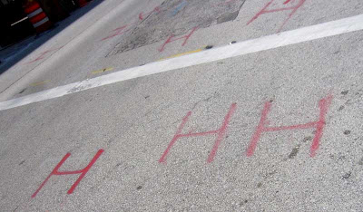 Red spray-painted shapes on asphalt look like H H H