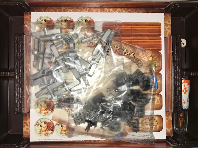 View inside the box when first opened. The cutlery is in two parts and in bags and the sheet of counters and trap covers is visible underneath
