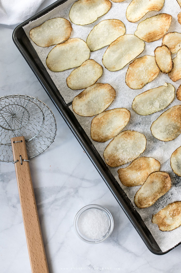 Potato chips drying on paper towel lined baking sheet with spider strainer.