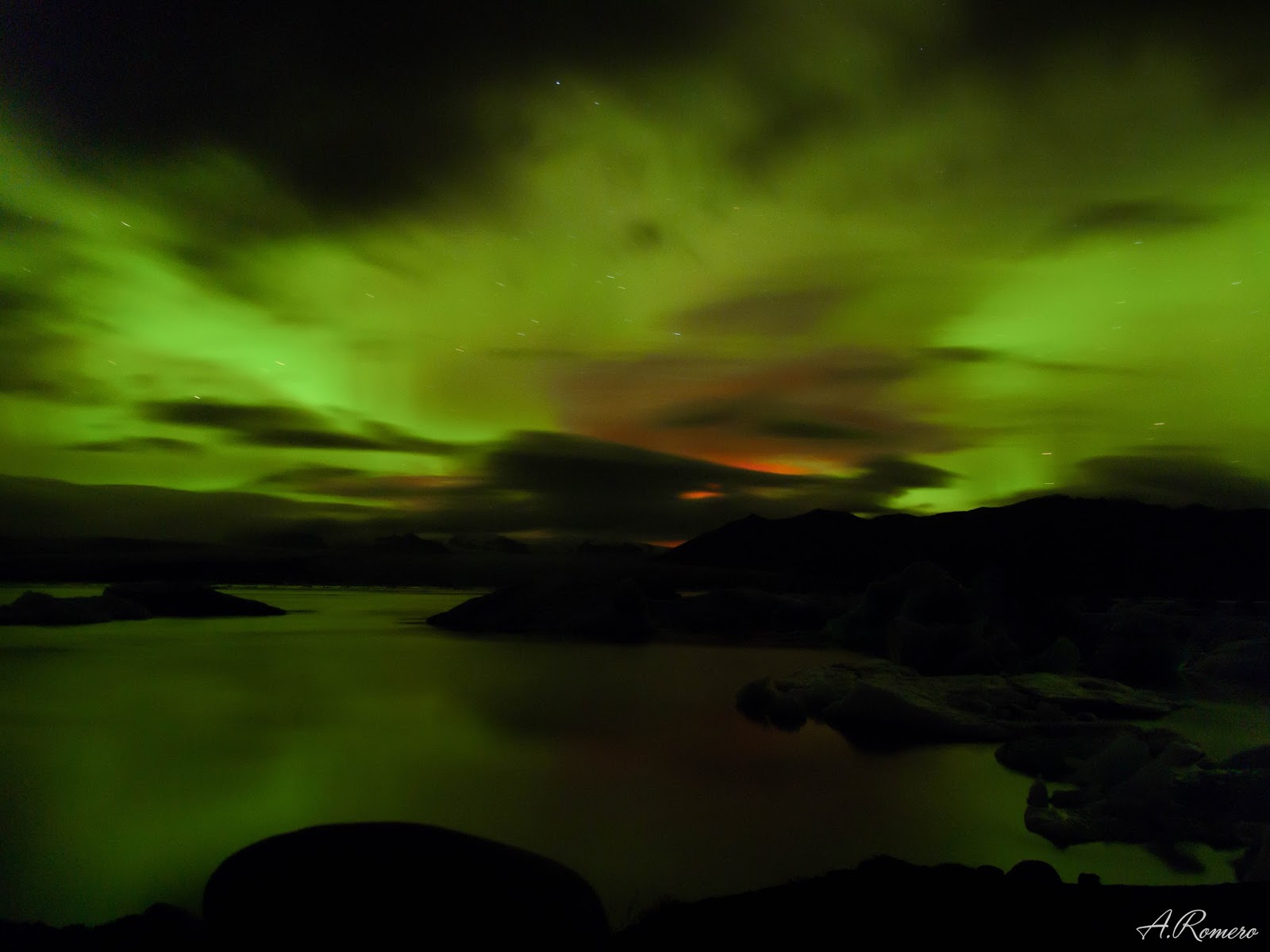 Una aurora boreal tiñe el cielo de verde reflejándose en la laguna glaciar Jökulsárlón. El resplandor anaranjado del horizonte lo produce el volcán Bárðarbunga que se encuentra activo bajo el mayor glaciar de Islandia.