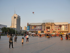 Girl flying kite at Culture Square (文化广场)  in Mudanjiang, China, with sign for the Guomao Shopping Center (国贸商城) in the background