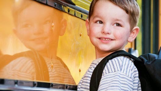 Criança com mochila ao lado de seu reflexo numa superfície plana vertical.