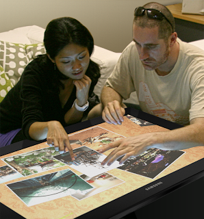Two tourists explore content while sitting at a digital table.
