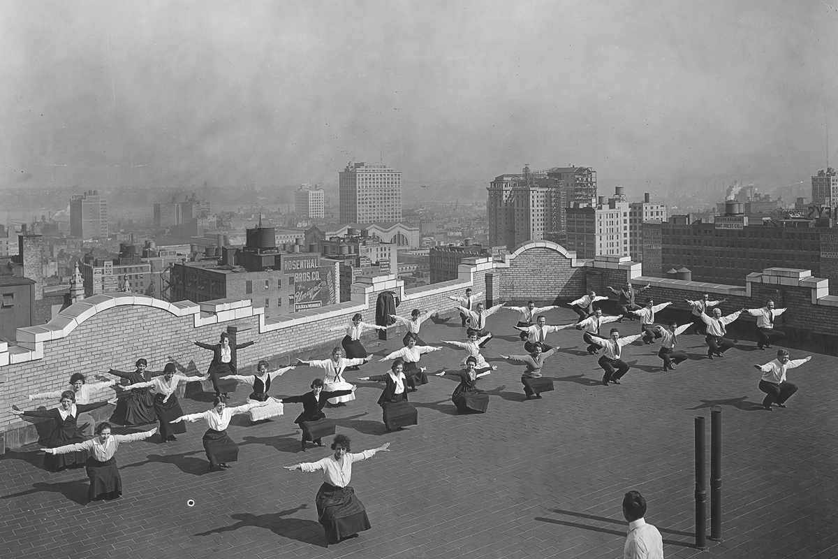 Original caption: Physical training twenty-two stories in the air. Men and girls employed by the New York State Industrial Commission going through physical exercises designed for the National Security League, on the roof of the Victoria Building in New York.