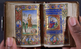 An open, miniature book of hours with densely painted and illuminated illustrations.