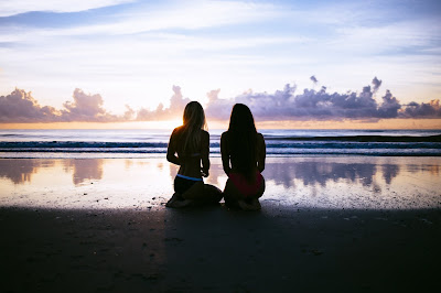 Dos chicas en biquini sentadas frente a el mar