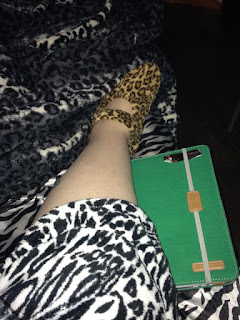 Author's pale leg with zebra satin sheets underneath, brown leopard print slipper, white leopard print bathrobe, white leopard print blanket, and green iPad case.