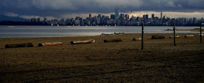 View of sandy beach, sailboats and freighters on English Bay and downtown Vancouver under an overcast sky