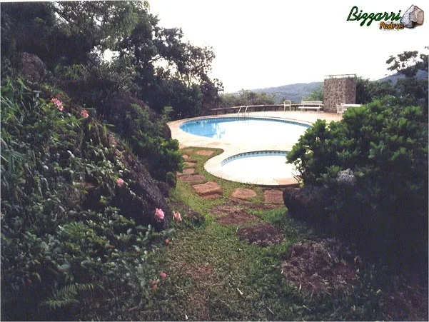 Muro de arrimo com pedras para apoiar a construção da piscina em uma área muito inclinada e os caminhos de pedra natural com junta de grama.