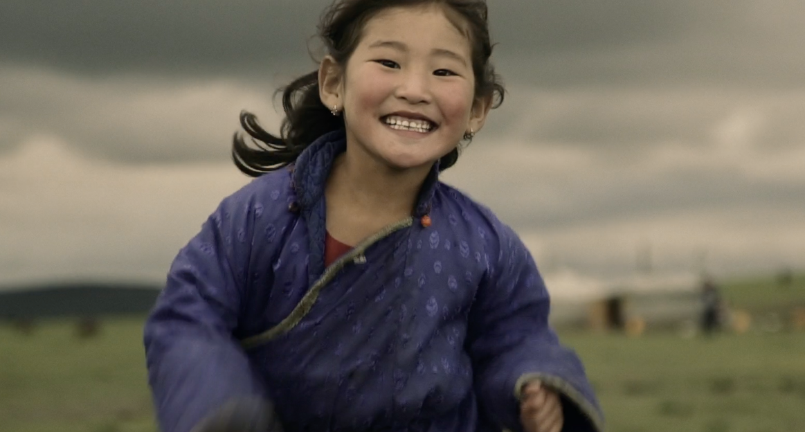 Ein mongolisches Mädchen rennt freudestrahlend auf den Betrachter zu. 