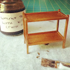 Stained modern miniature tea trolley on a workbench with a jar of diluted walnut stain  next to it and a brush in front of it.