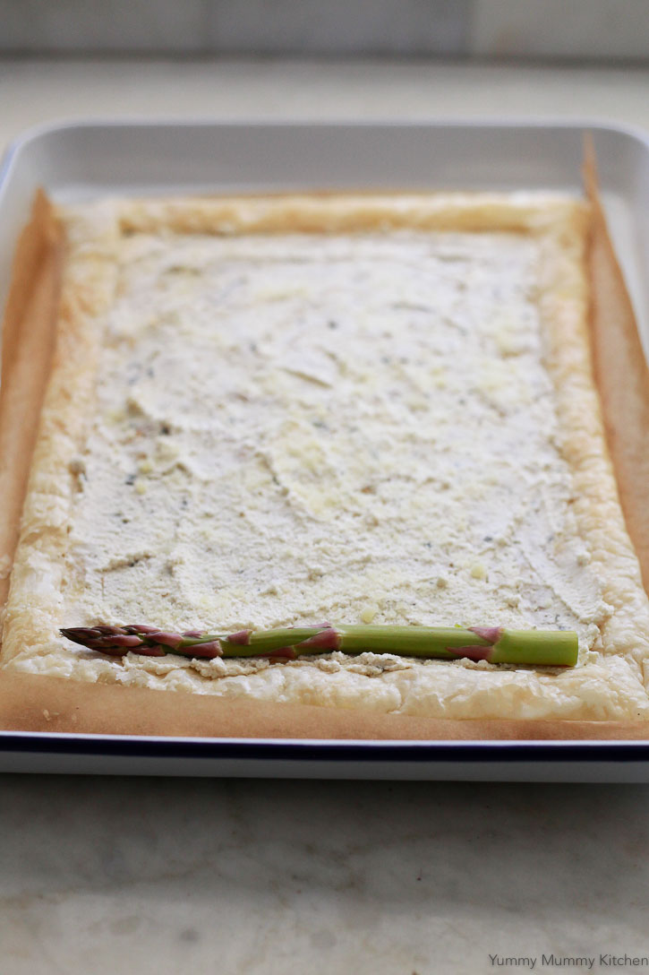 Par-baked puff pastry with a layer of soft cheese as it gets topped with fresh asparagus. 