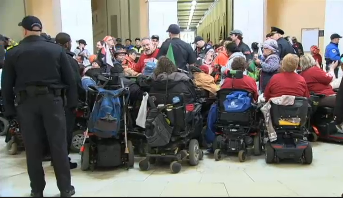 Protesters in wheelchairs viewed from behind, indoors