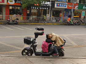 girl resting while sitting on the back of a parked motor scooter