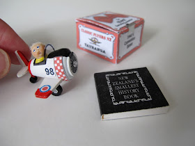 Ornament of a boy in a pedal plane, with a miniature book next to it. A hand shows scale.
