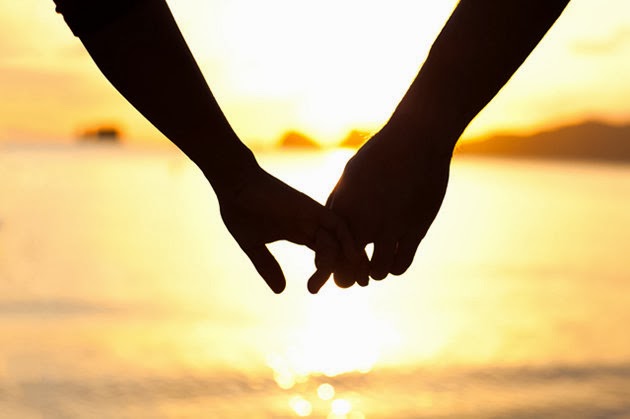 As mãos de um casal frente ao lindo por do sol em uma praia deserta