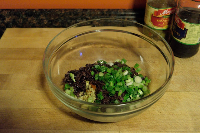 Chopped green onions being added to the chopped olives in the bowl. 