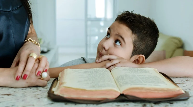 Menino olha sua mães que o ensina sobre a Bíblia sagrada sobre a mesa