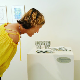 Woman looking at small porcelain buildings in a gallery.