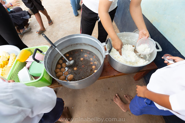 Lunch for these Cambodian Children today is rice, eggs and pineapple. Being served outside the school. The children line up. The teachers serve from large tin pots.